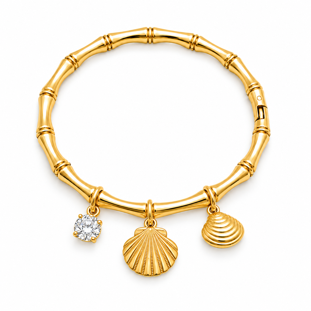A gold charm bracelet styled like a bamboo stalk, featuring three dangling charms: a textured scallop shell, a smaller ribbed shell, and a round clear gemstone charm, shown on a plain white background.