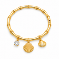 A gold charm bracelet styled like a bamboo stalk, featuring three dangling charms: a textured scallop shell, a smaller ribbed shell, and a round clear gemstone charm, shown on a plain white background.
