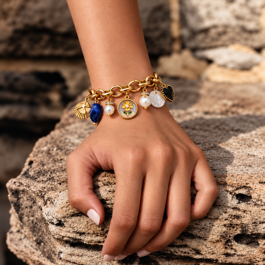 A gold charm bracelet with multiple decorative pendants, worn on a person's wrist and resting on a textured stone surface.