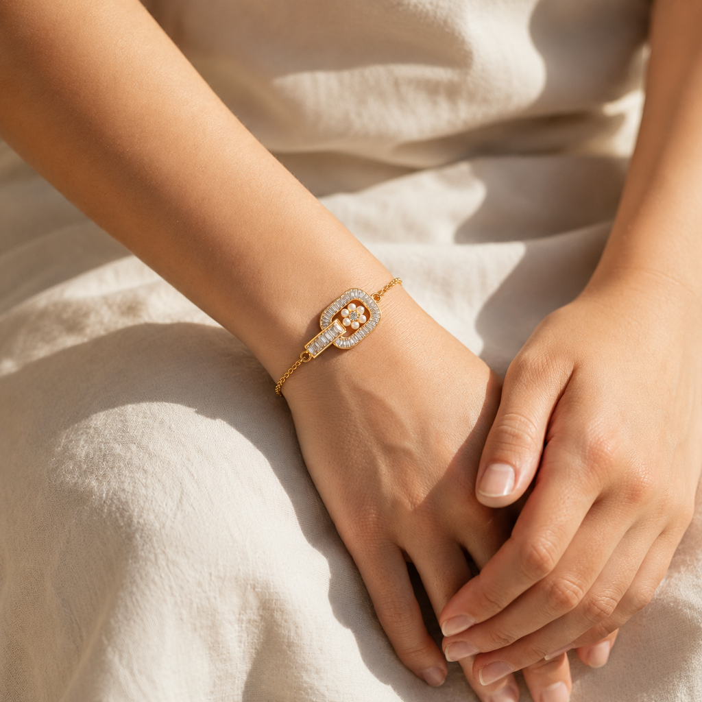 A delicate gold bracelet with a central cluster of white pearls and pavé-set clear stones, shown worn on a person's wrist against a soft beige linen background.
