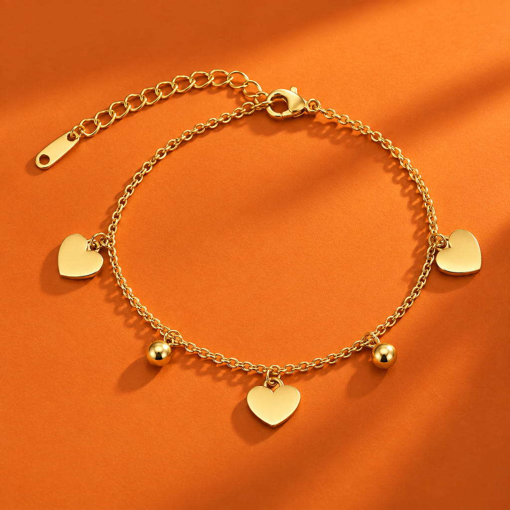 A gold chain anklet with three heart charms, two small heart beads, and an adjustable lobster clasp, displayed on a textured orange background.