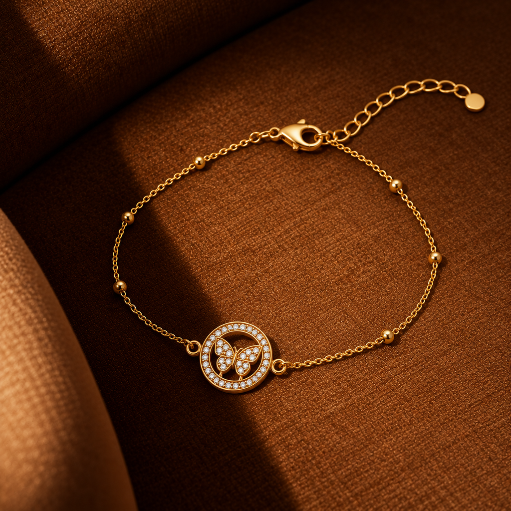 A delicate gold chain bracelet with a circular butterfly pendant, set against a textured brown background.