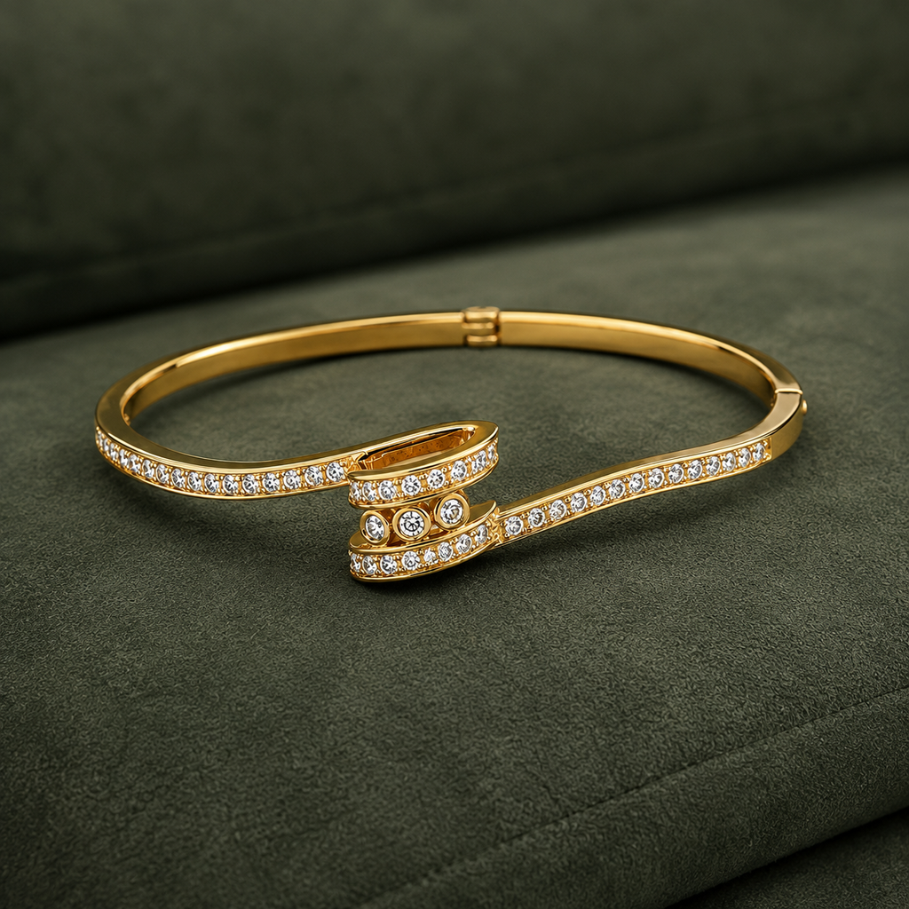 A gold hinged bangle bracelet with pavé-set clear stones, displayed on a dark olive green textured fabric background.
