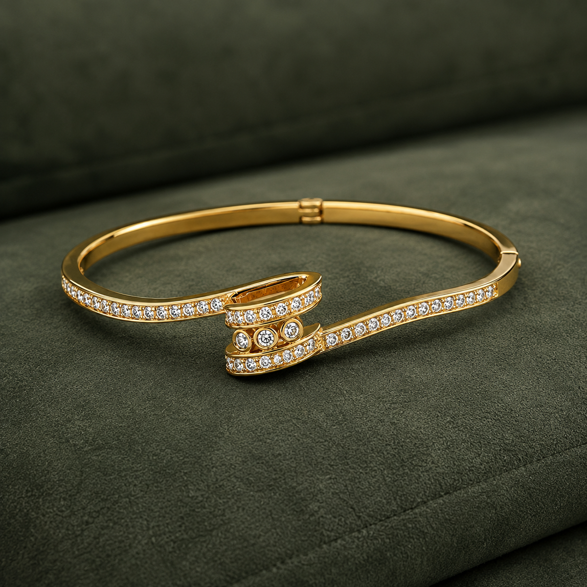 A gold hinged bangle bracelet with pavé-set clear stones, displayed on a dark olive green textured fabric background.