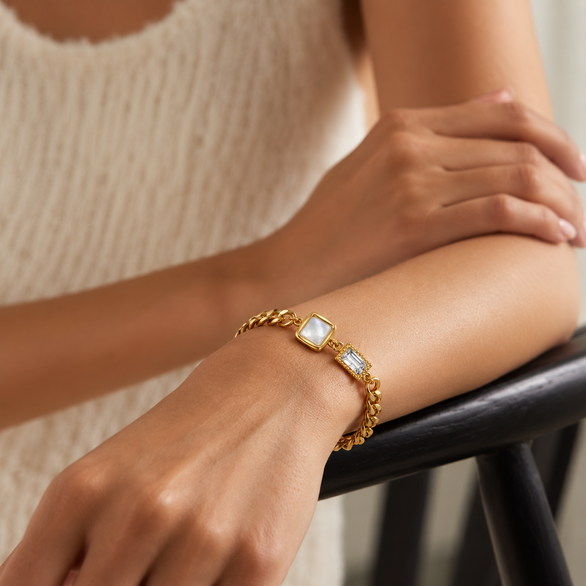 A gold chain bracelet with two rectangular white mother-of-pearl cabochons worn on a woman's wrist, shown in a close-up lifestyle shot.