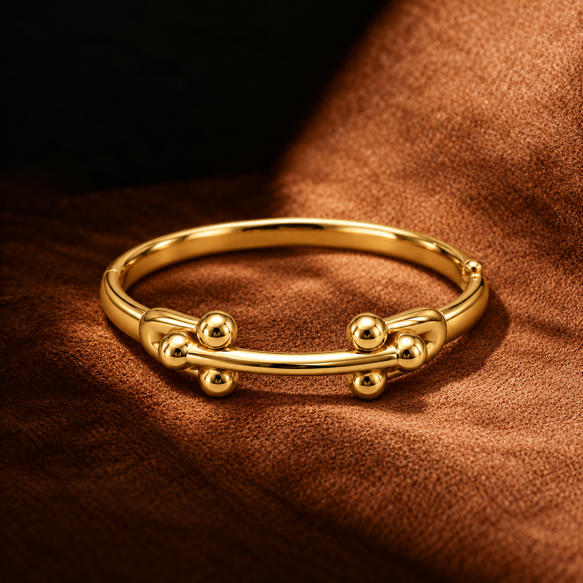 A polished gold bangle bracelet with decorative bead details, resting on a textured brown fabric background.
