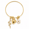 Gold bangle bracelet with dangling charms including a heart, a flower, a snake, and small gold beads, shown on a plain white background.
