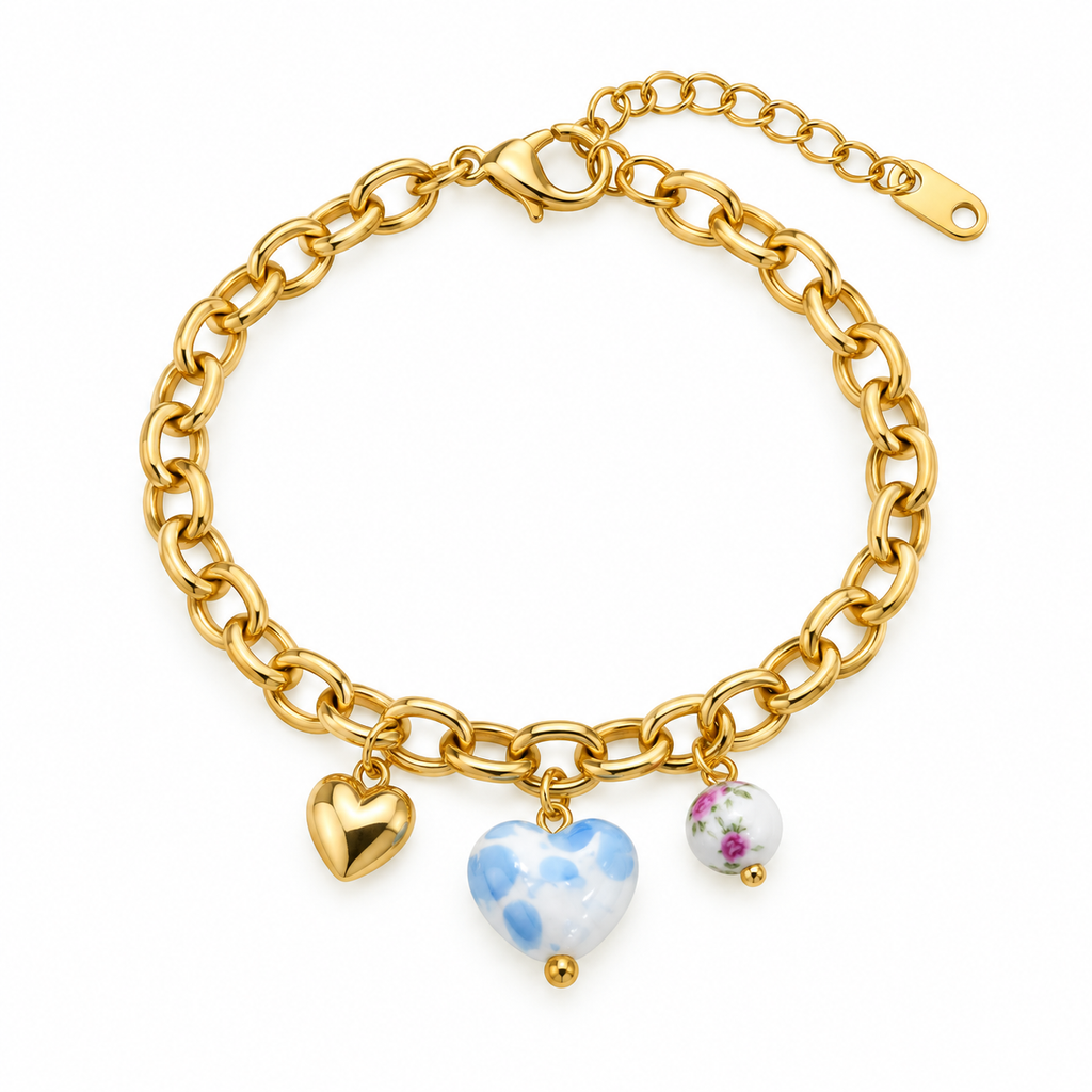 A gold chain charm bracelet featuring three heart-shaped charms: a plain gold heart, a blue and white marbled heart, and a small white heart with a floral print, set against a plain white background.