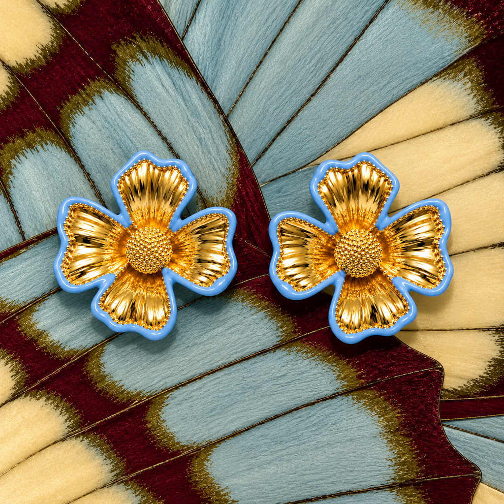 A pair of gold flower-shaped earrings with textured petals and a light blue border, displayed on a large butterfly wing background.