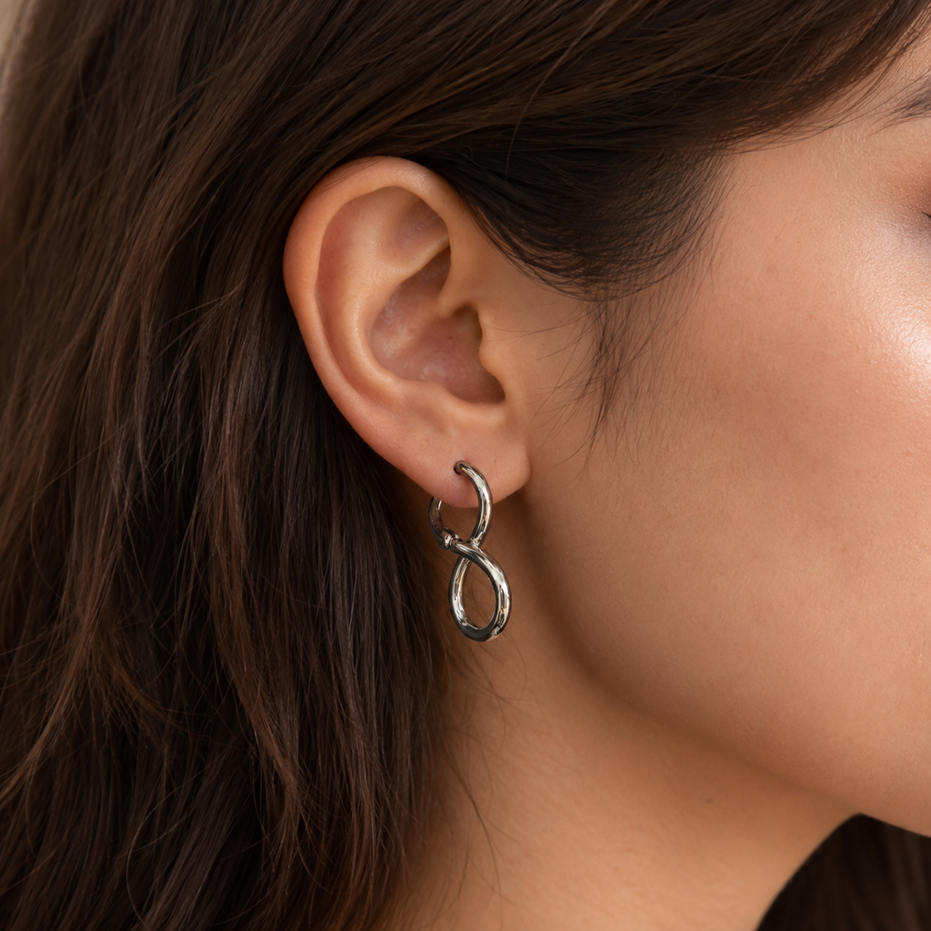 A close-up of a model's ear wearing a small silver infinity-shaped hoop earring.
