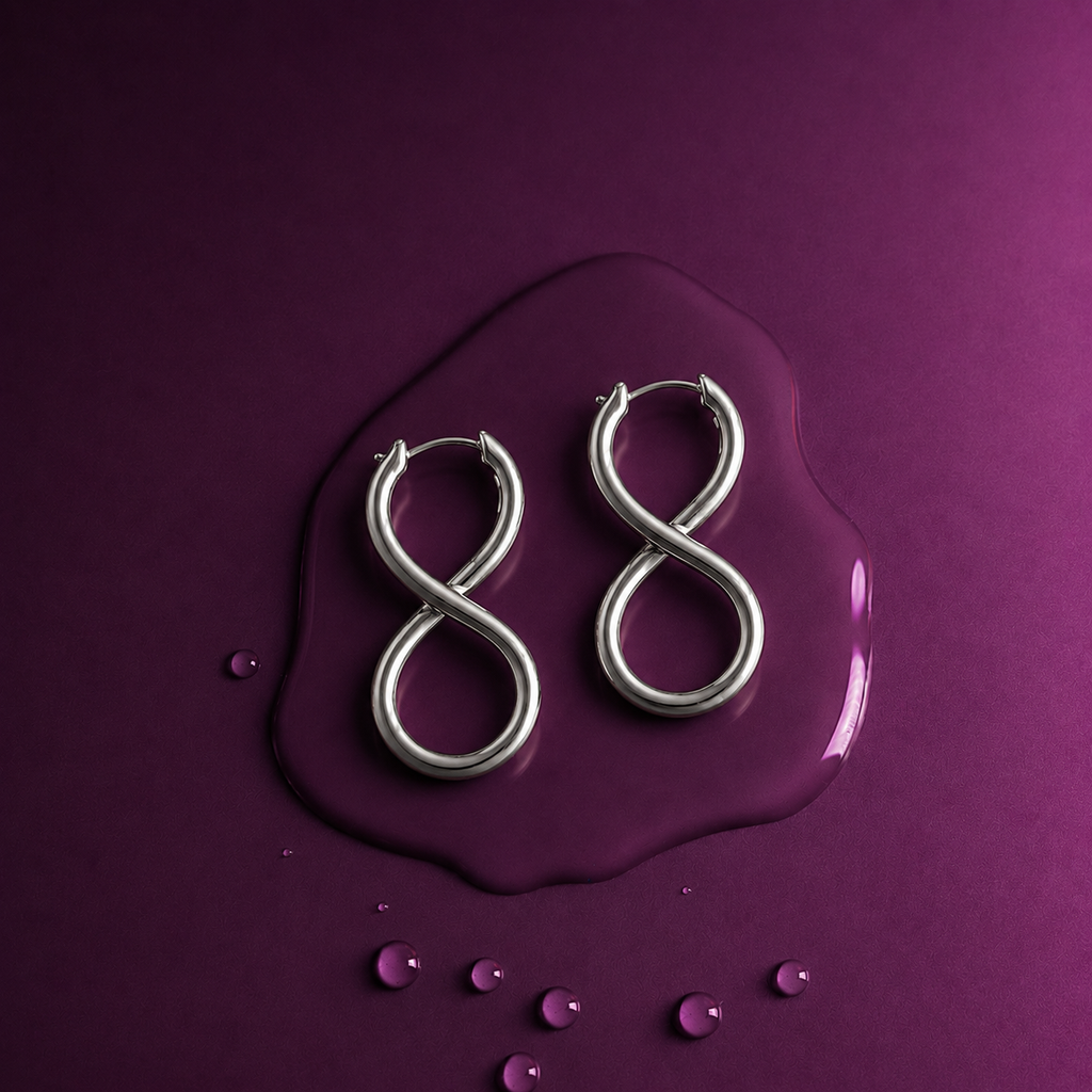 A pair of silver hoop earrings shaped like the number 8, displayed on a glossy purple puddle with small scattered droplets on a solid purple background.