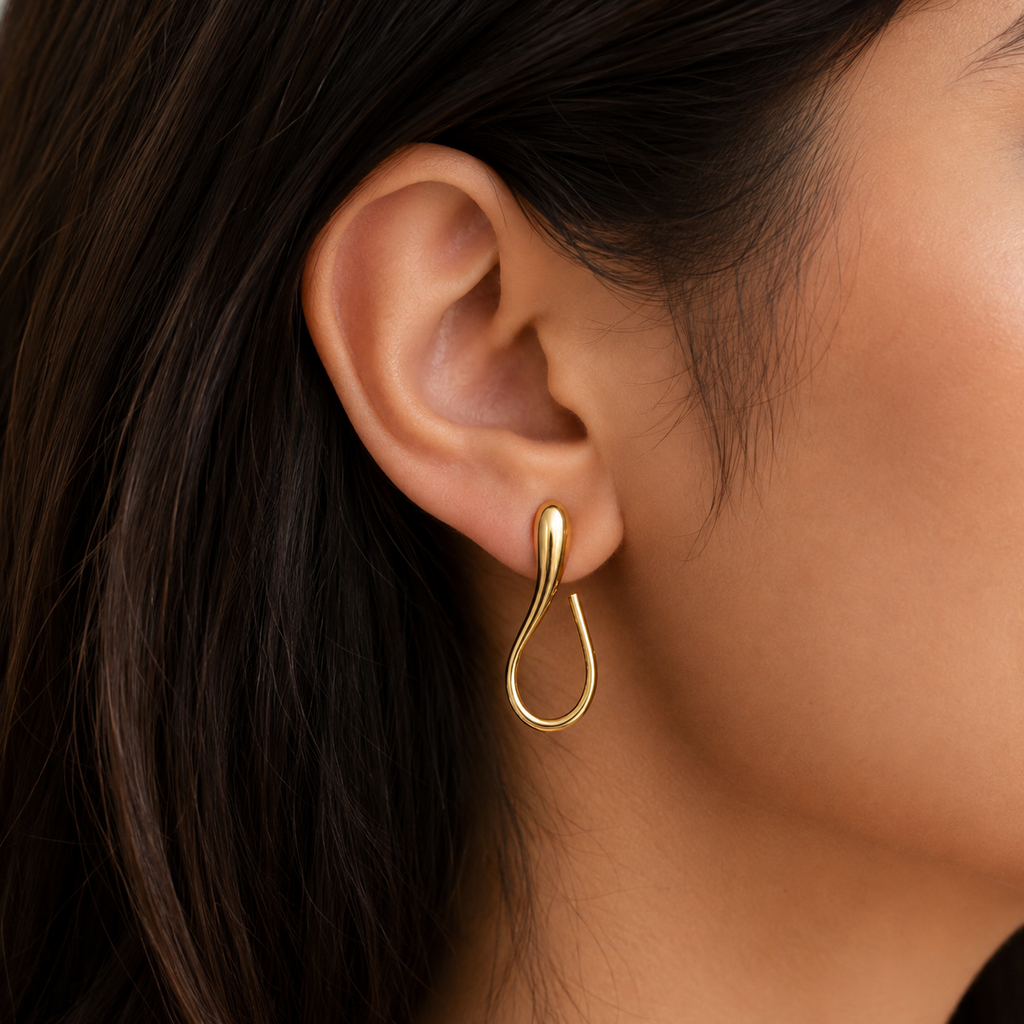 A close-up of a model's ear wearing a polished gold teardrop-shaped hoop earring.