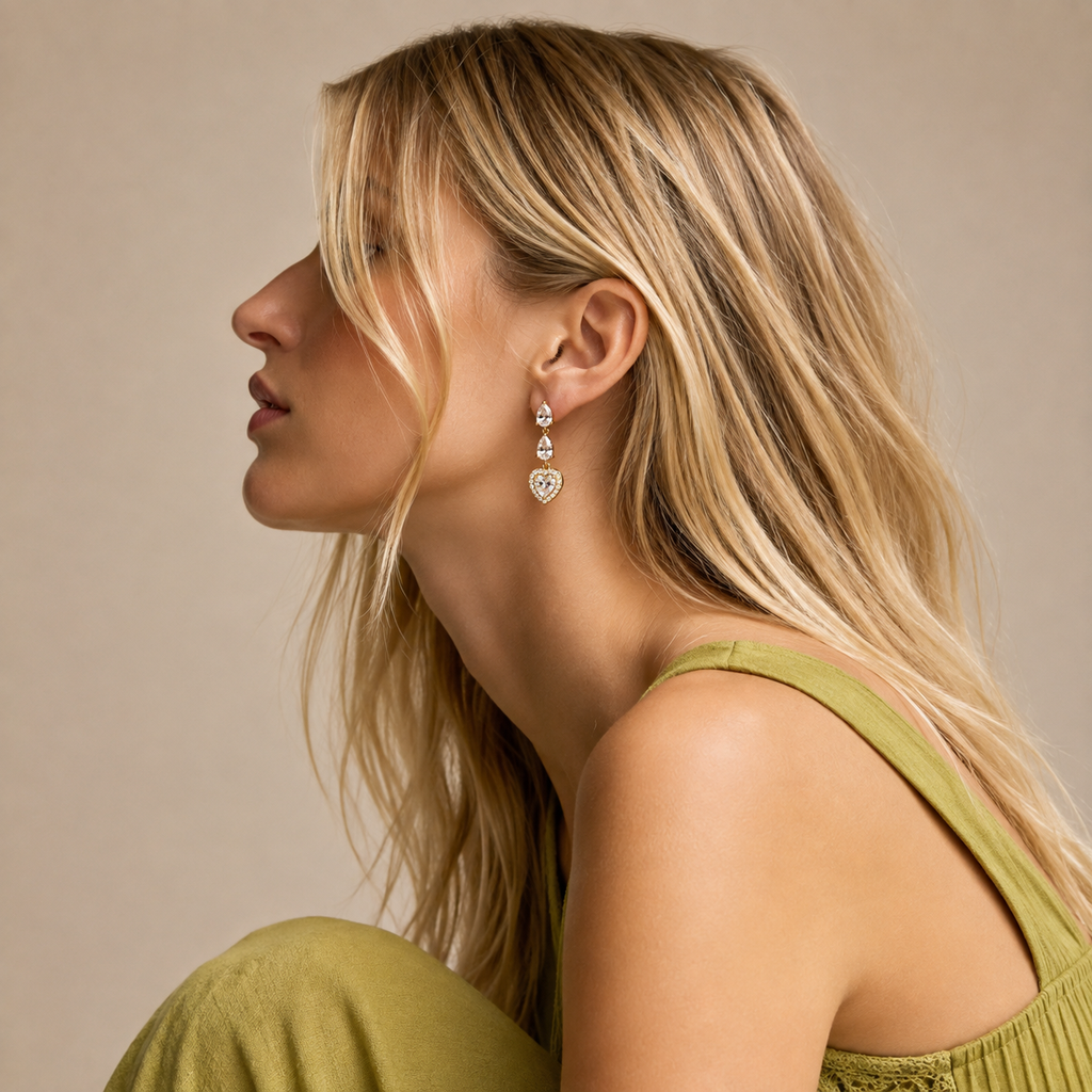 A woman in profile wearing a gold heart-shaped dangle earring with clear gemstones, against a warm beige background.