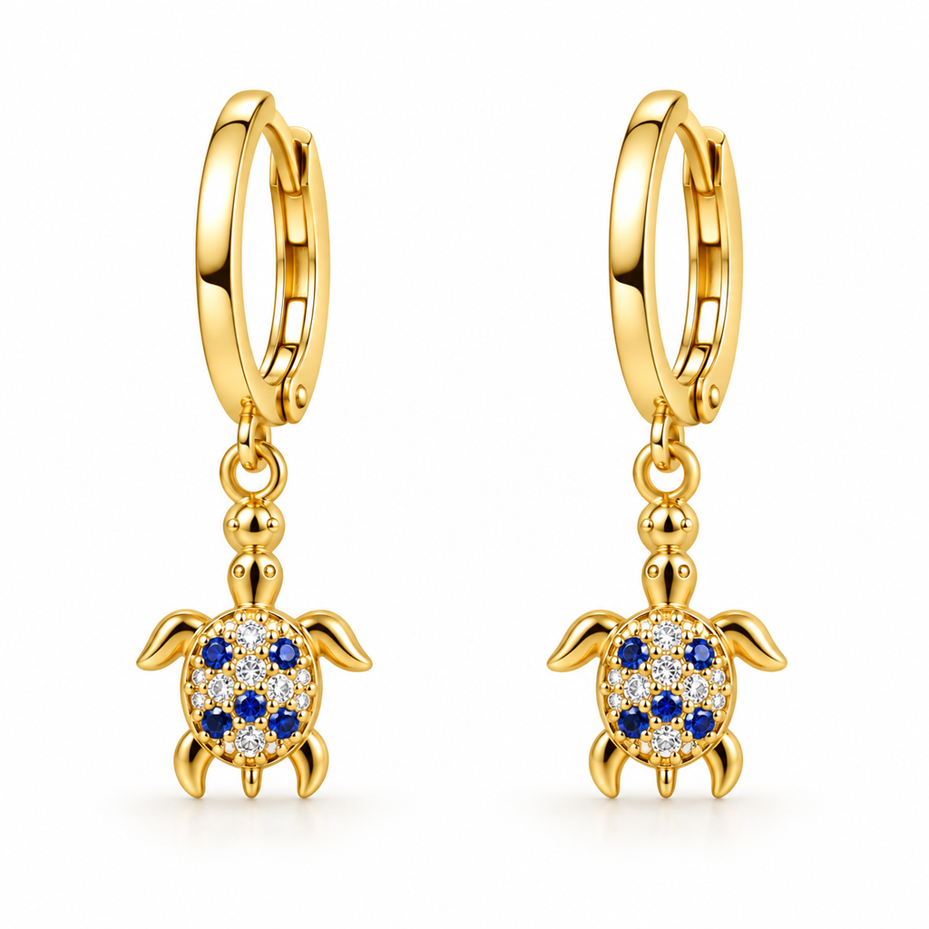 A pair of gold huggie hoop earrings with dangling turtle charms. The turtle charms feature blue sapphires set in a halo of clear pavé stones, shown on a clean white background.