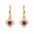 A pair of gold huggie hoop earrings with clover-shaped drops, featuring a central round purple gemstone surrounded by a halo of small clear stones, on a plain white background.