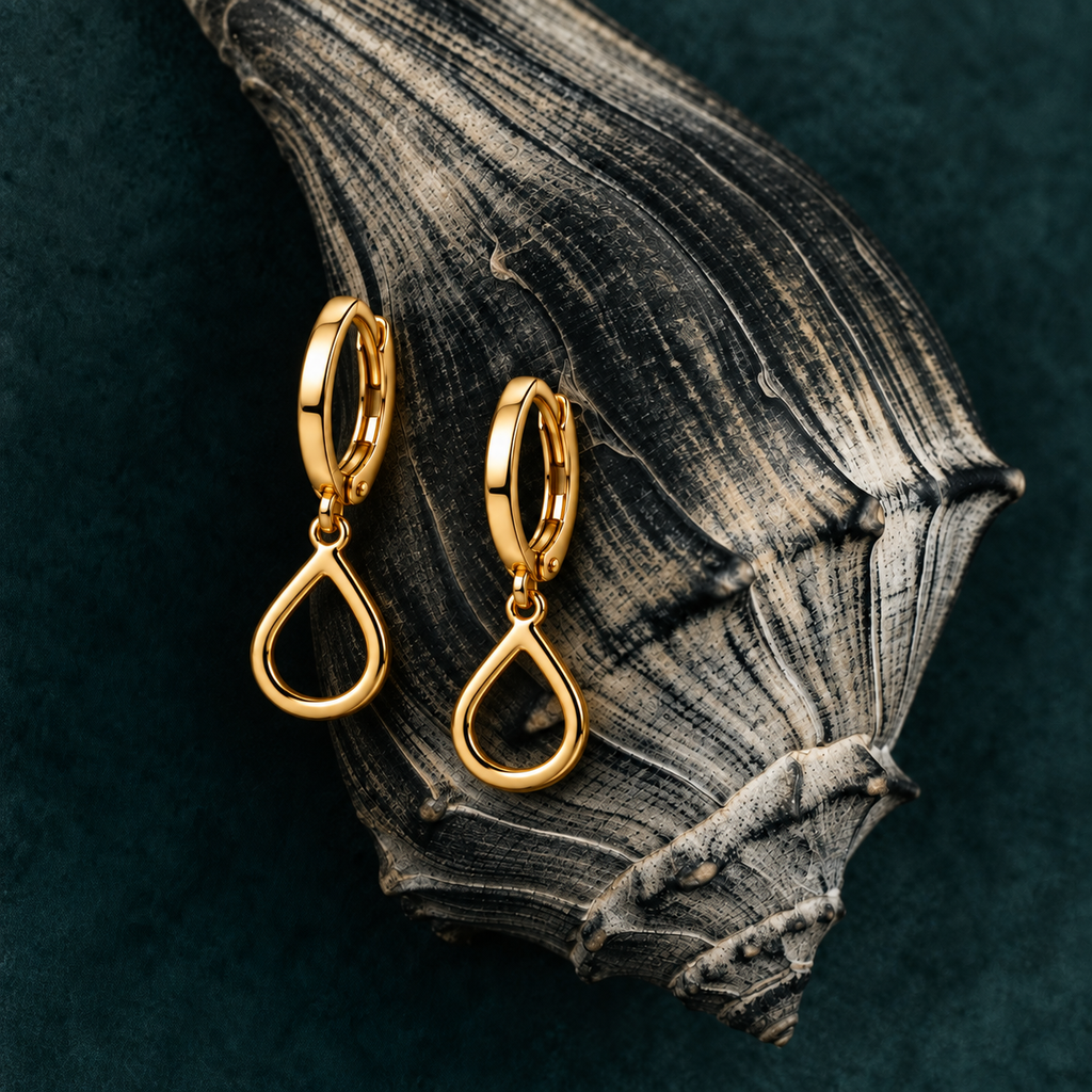 A pair of gold hoop earrings with open teardrop-shaped dangles, displayed on a textured dark wood slice over a deep teal background.