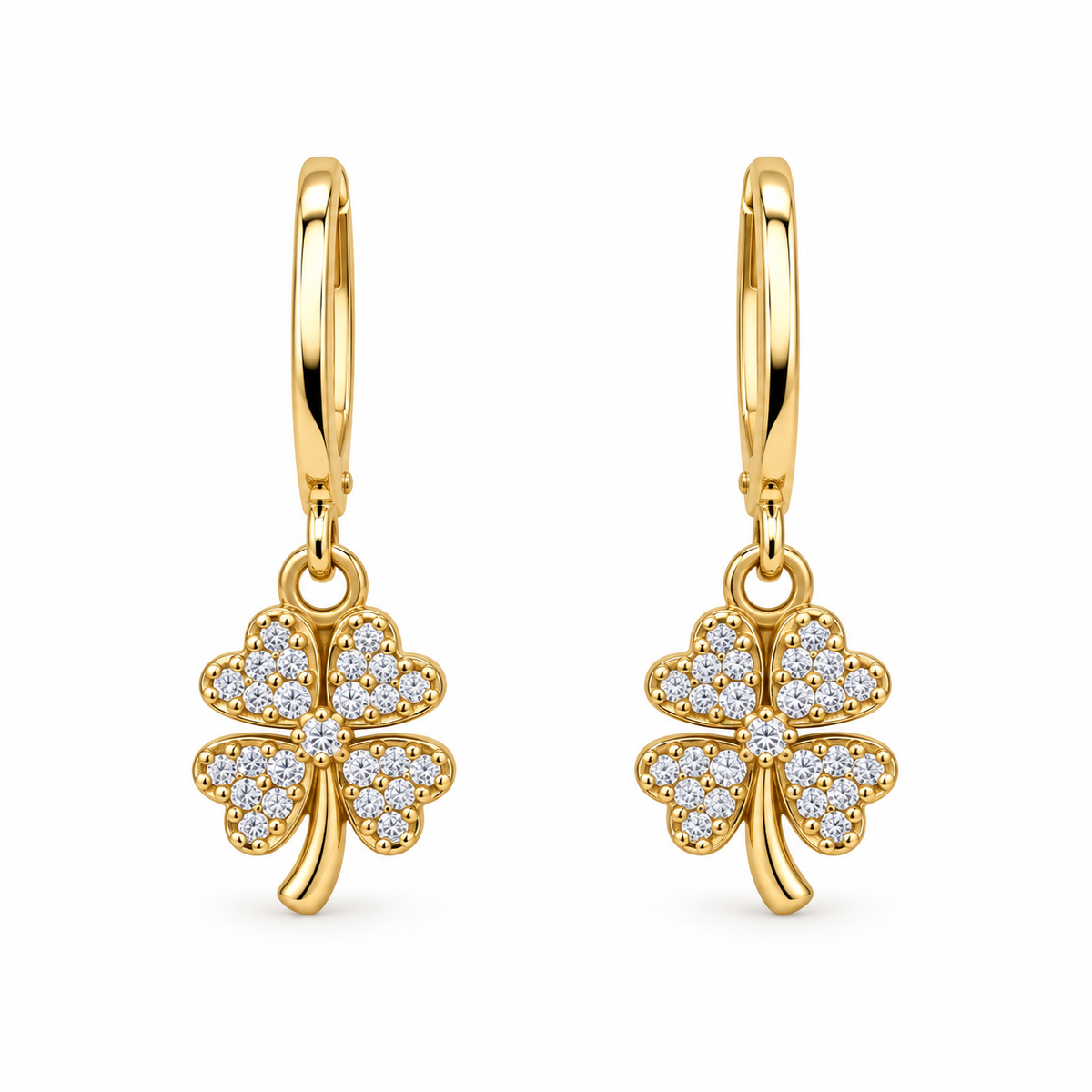 A pair of gold hoop earrings with dangling four-leaf clover charms paved with small clear stones, shown on a plain white background.
