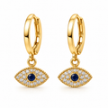 A pair of gold huggie hoop earrings with dangling evil eye charms. The charms feature a central round dark blue stone surrounded by a halo of small clear stones, all set in polished yellow gold, shown against a plain white background.