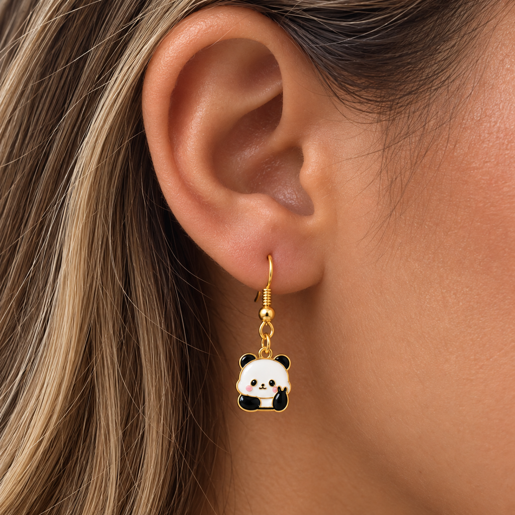 A close-up of a person's ear wearing a gold-toned dangle earring with a panda charm. The charm features white, black, and pink enamel details.