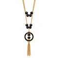 A gold-tone and black beaded necklace featuring a circular pendant with a central black bead, flanked by small gold beads, and finished with a dangling gold-tone tassel chain, shown on a plain white background.