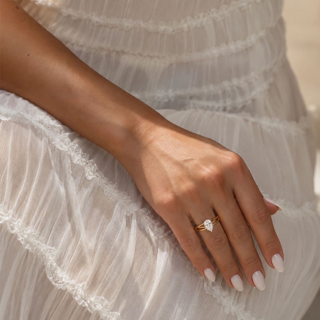 A close-up of a person's hand resting on a white ruffled dress, wearing a delicate gold ring with a small white stone.
