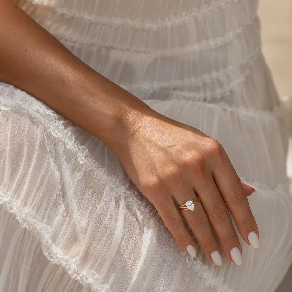 A close-up of a person's hand resting on a white ruffled dress, wearing a delicate gold ring with a small white stone.