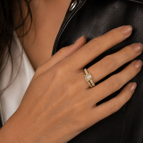 A close-up of a hand wearing a gold ring with a rectangular clear gemstone, resting against a black leather jacket.