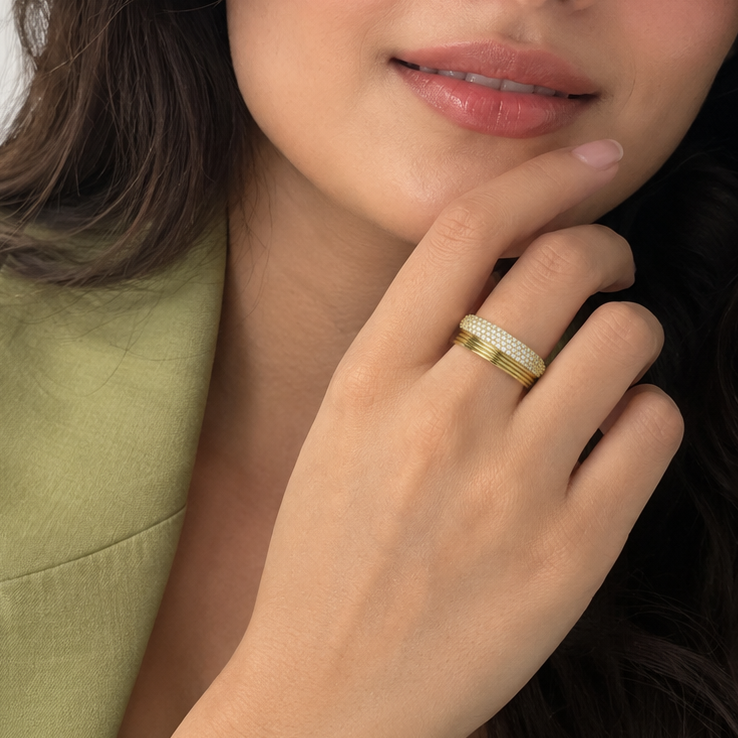 A close-up lifestyle shot of a woman wearing a gold band ring with a row of small white stones, resting her chin on her hand.